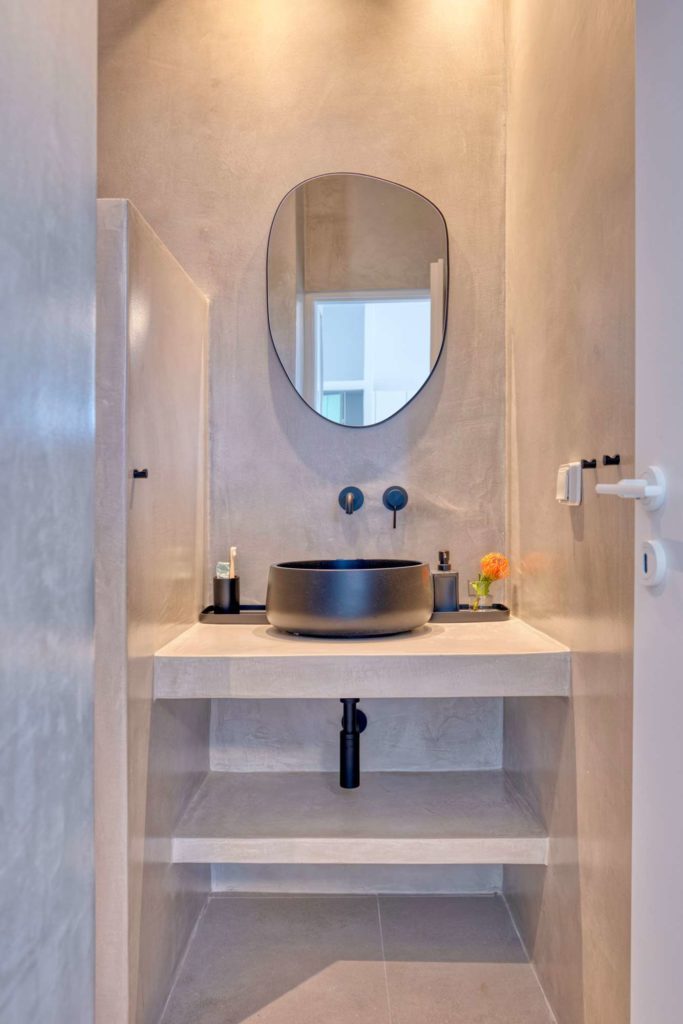 Microcement bathroom with an oval mirror, dark stone basin and open shelving