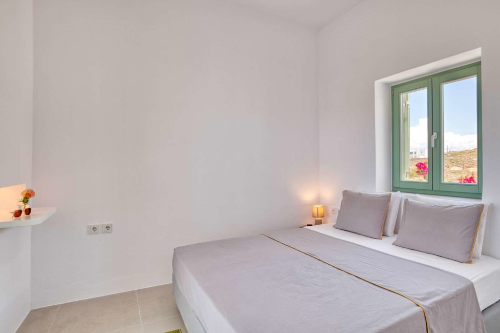 The bedroom at dusk with a bedside lamp lit and the window to the sea