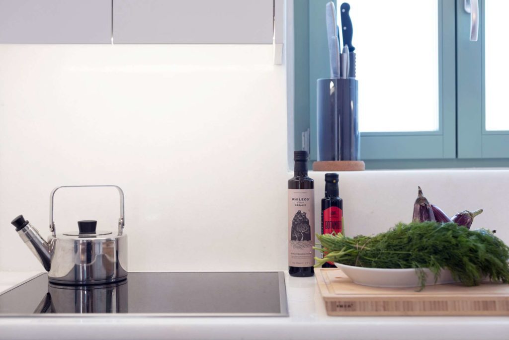 Kitchen counter with hob, kettle, olive oil and fresh herbs on a board