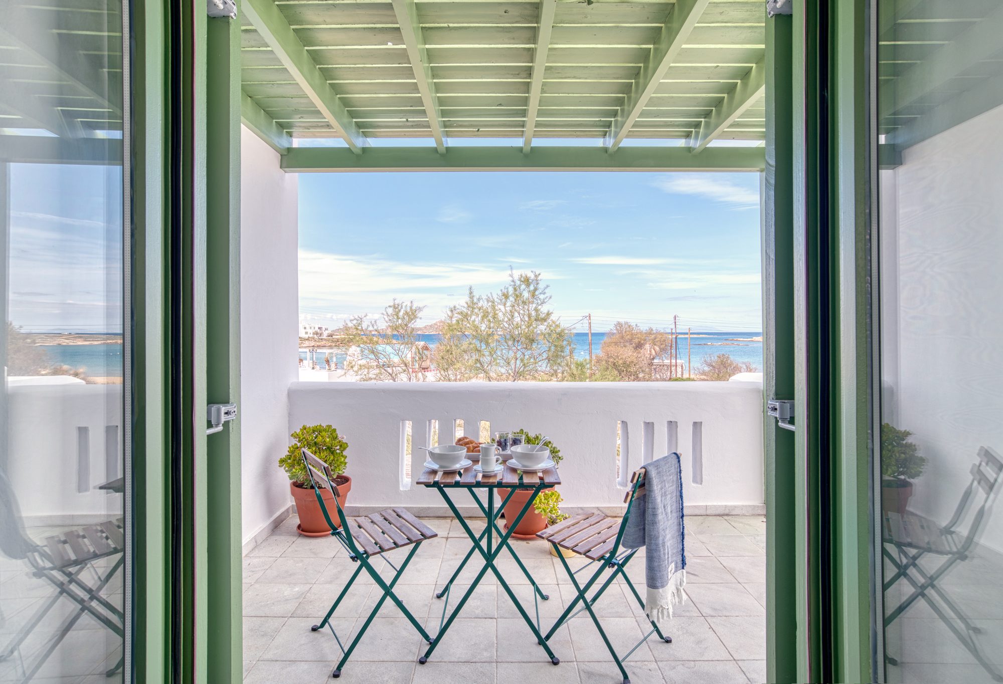 The open green doors of the apartment looking out across the terrace table to the sea