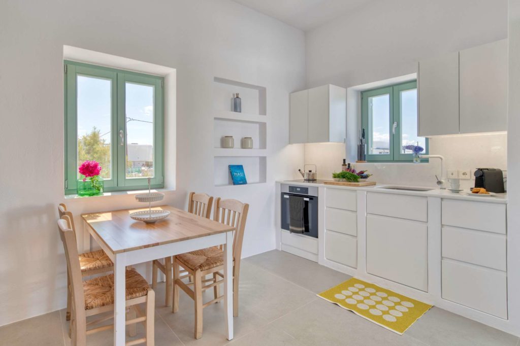 The white kitchen and wooden dining table for four, with green-framed windows
