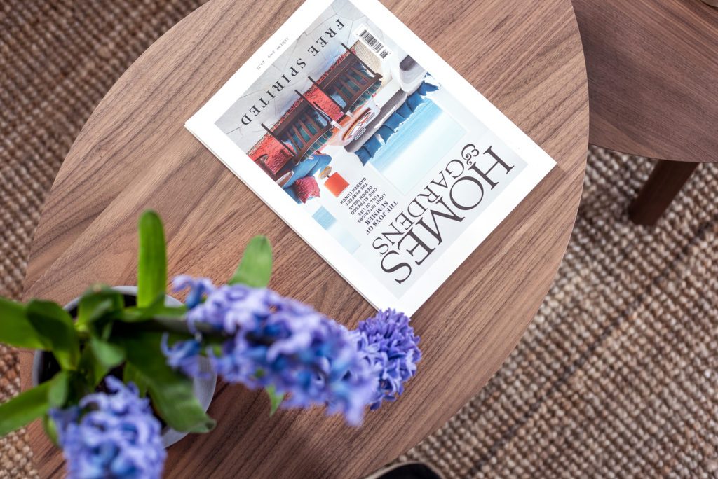 A vase of blue hydrangeas beside a magazine on the round walnut table