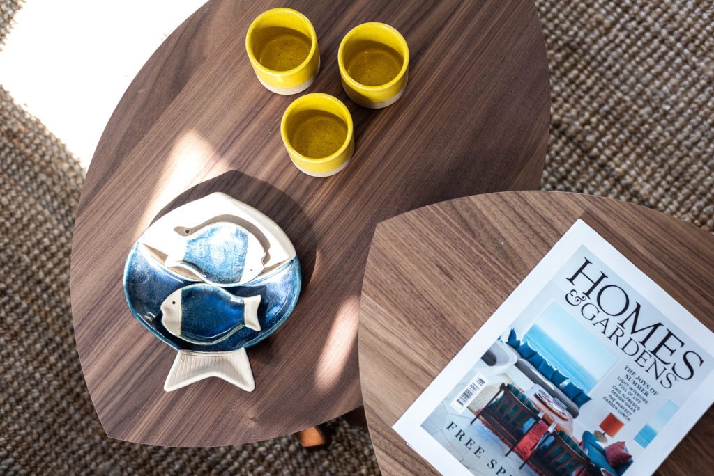 Walnut coffee tables with yellow espresso cups, a ceramic fish dish and a magazine