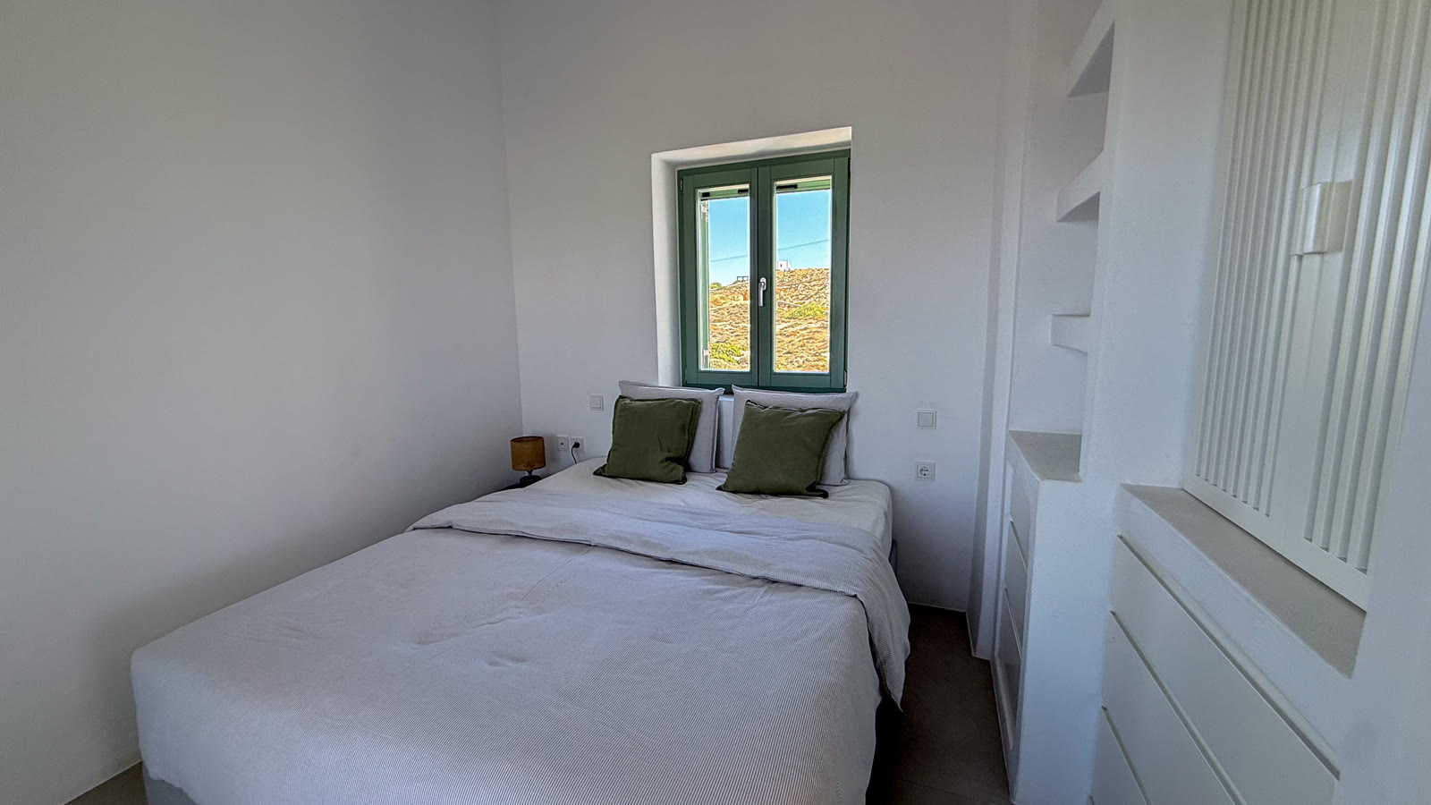 The queen bedroom with fresh white linen and a green-framed sea-view window