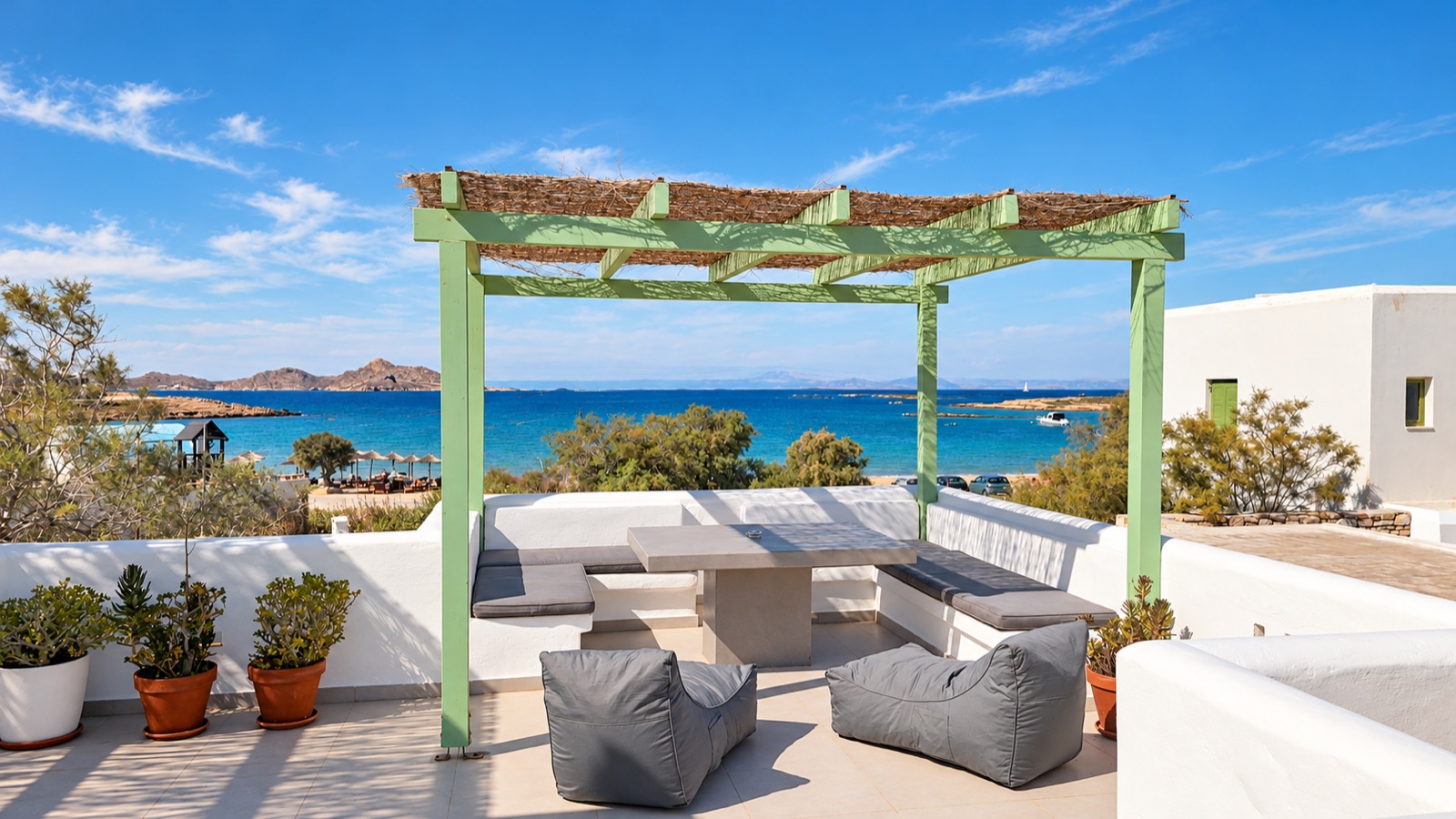 May Lola's sunlit terrace beneath its sage-green pergola, overlooking Agioi Anargyri bay